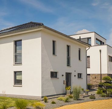 Moderne zweistöckige Häuser mit minimalistischem Design, weißen Fassaden und einer begrünten Umgebung unter einem klaren blauen Himmel.