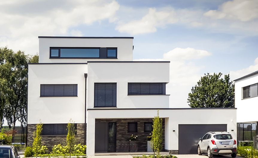 Modernes zweistöckiges Haus mit schlichtem weißem Äußeren, großen Fenstern, Steinakzenten und einer Einfahrt für ein geparktes Auto unter blauem Himmel.